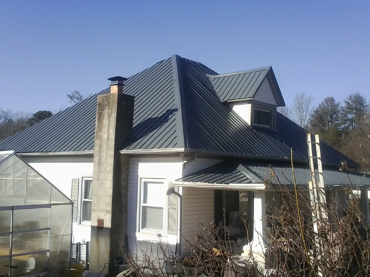 Dark blue standing seam metal roof on a white farmhouse with dormer — Slate & Tile Roof Repair by Roofing Brothers in Englishtown