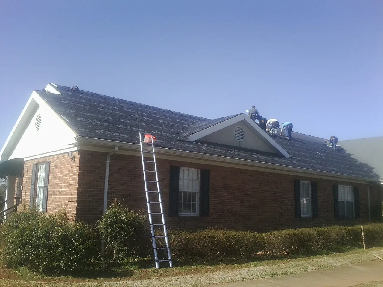 Crew tearing shingles off a brick ranch roof with a ladder set — Emergency Roof Repair work by our crew in Englishtown