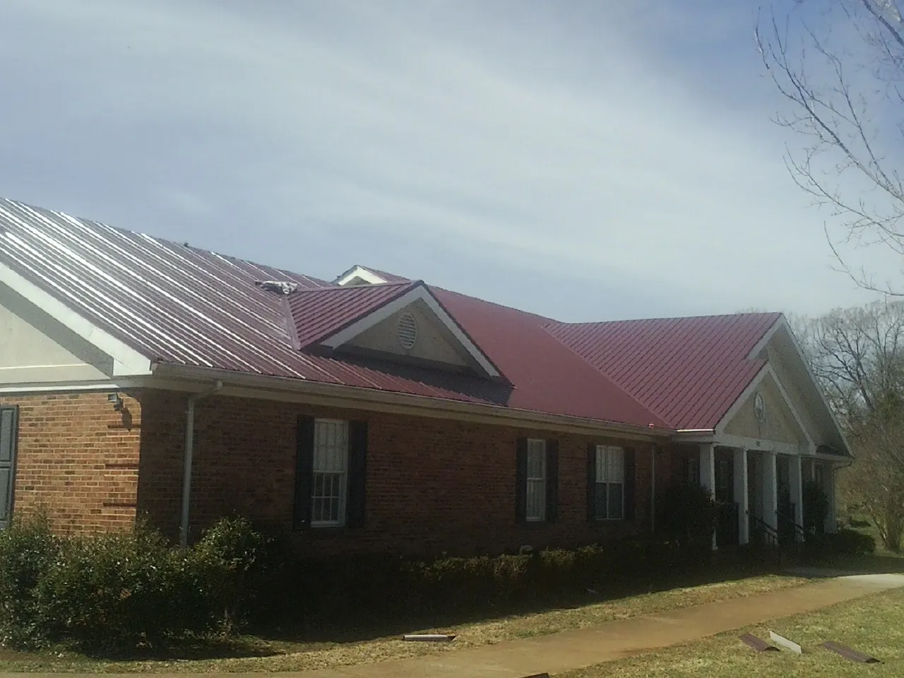 Red metal roof with gabled entries on a long brick building, from a Hail Damage Roof Repair job in Englishtown