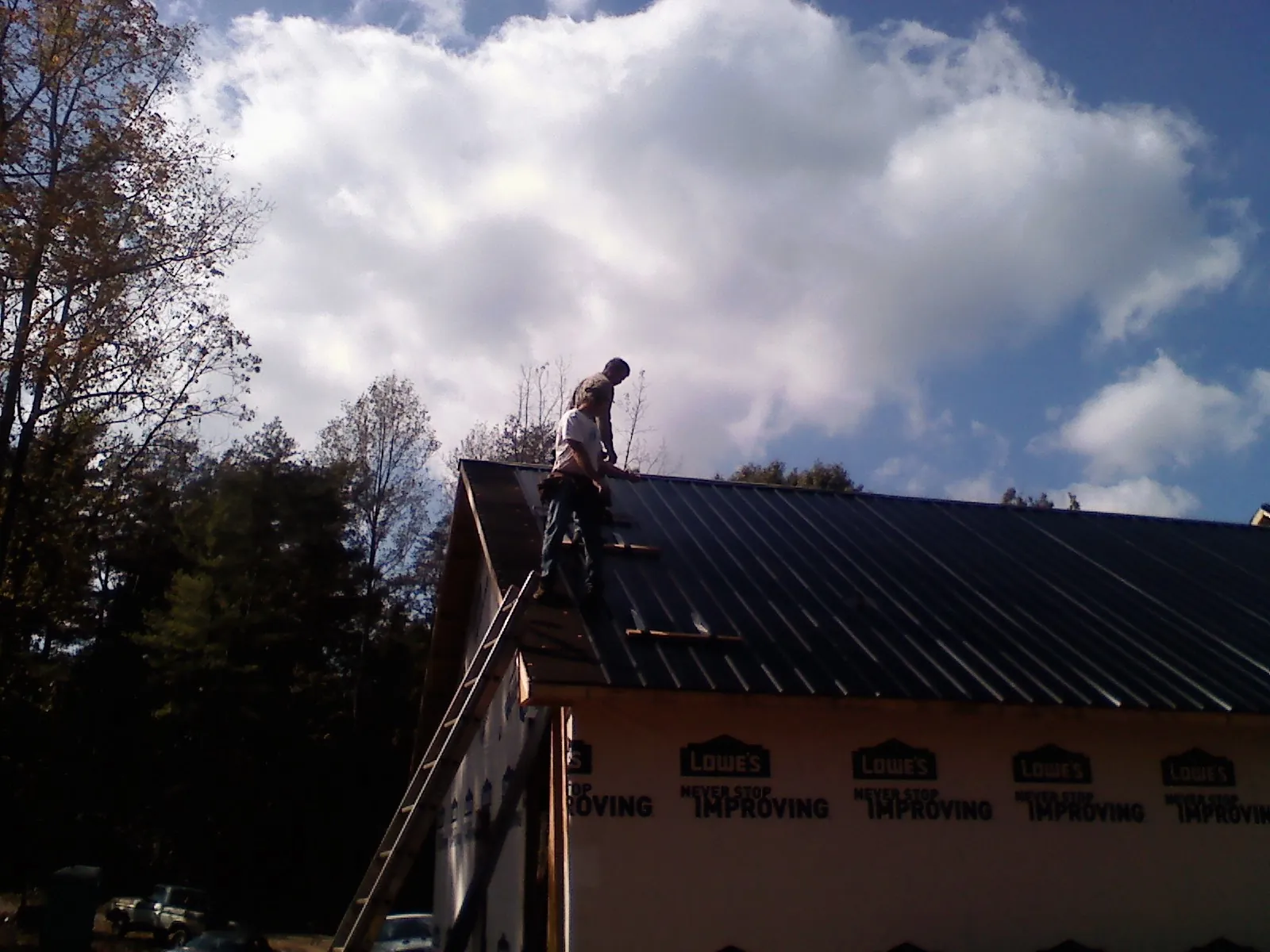 Roofer fastening dark metal panels high against a cloudy sky, from a Roof Inspection job in Englishtown