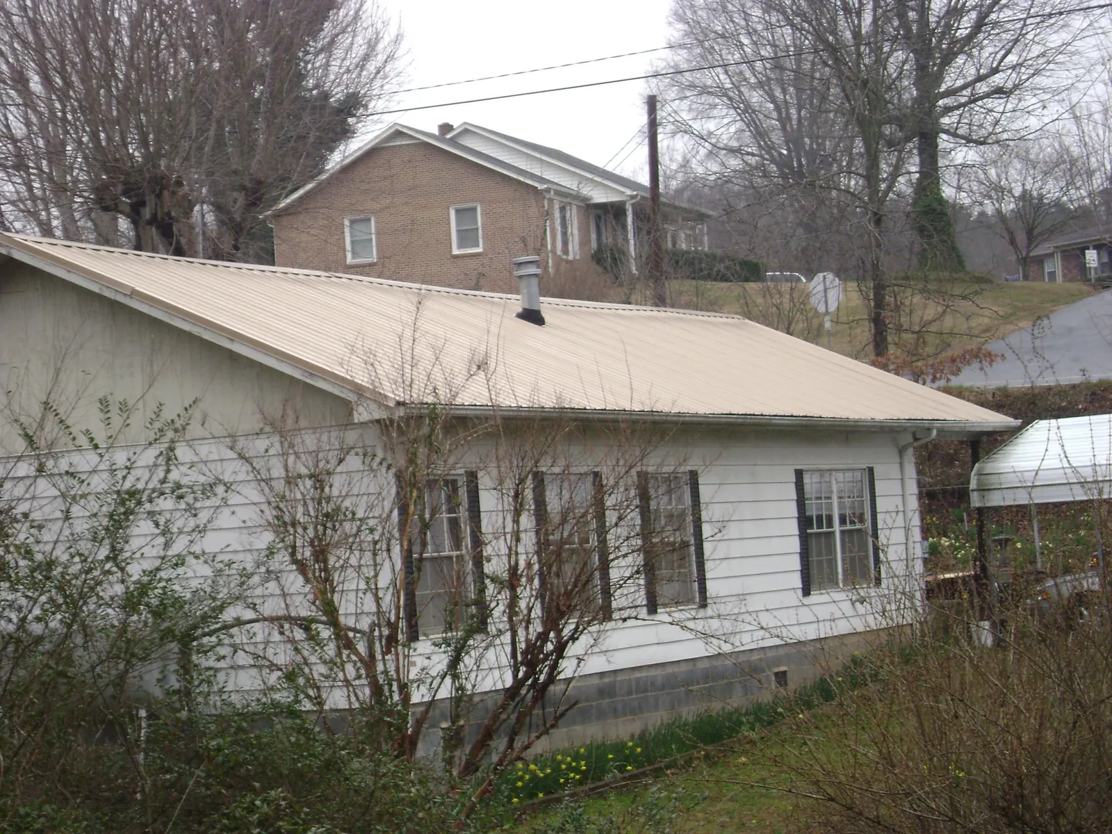 Tan metal roof on a white sided house set into a hillside — Commercial Roofing by Roofing Brothers in Englishtown